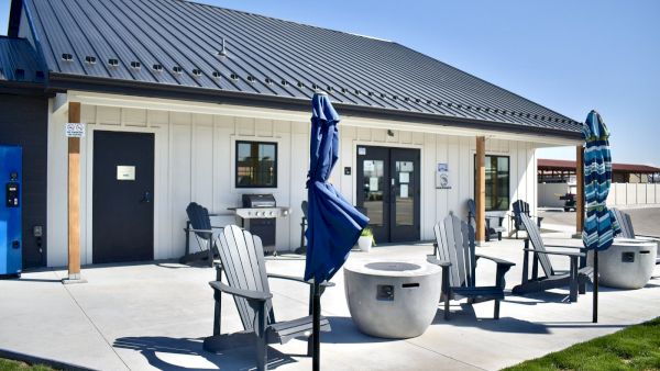 An outdoor seating area with Adirondack chairs, umbrellas, and a concrete patio in front of a modern building under a sunny blue sky.