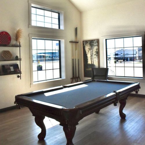 A billiards room featuring a full-size pool table, large windows, and wall art in a bright, minimalist space.