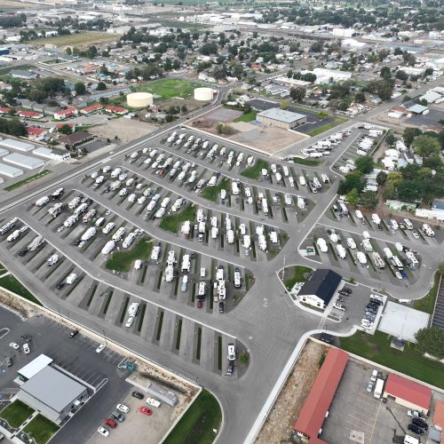 An aerial view of a modern campus or business park with multiple gray-roofed buildings, parking lots, and surrounding green spaces, top it.