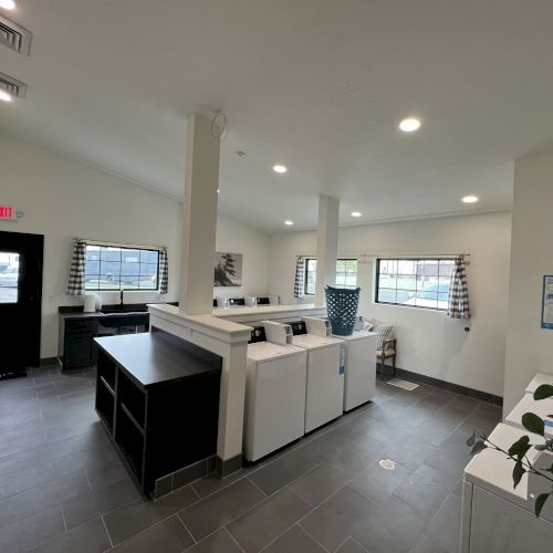 A modern, open-concept living space with a white kitchen island, dark flooring, ceiling lights, and a cozy seating area, airy and bright.