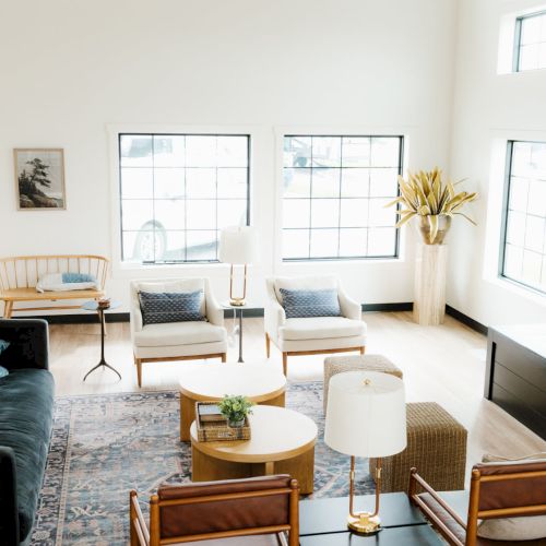 Cozy living room with a big window, wooden chairs around a small table, and a bright, airy look&mdash;rug, plants, and soft natural light.