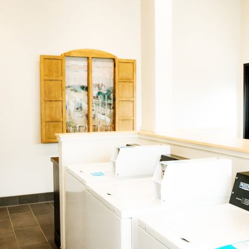 A bright laundry room with white cabinets, a wooden wall cabinet, a countertop, and a washing machine; clean and minimal.