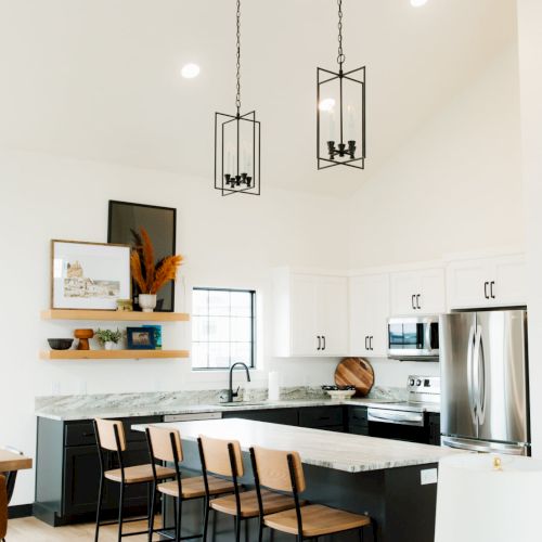 A bright, modern kitchen with a white island, sleek black bar stools, pendant lights, wooden accents, and minimal decor.