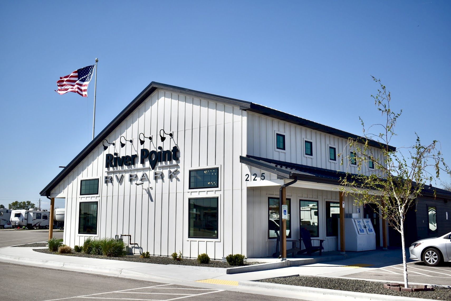 Rural-style building with a small sign &ldquo;River Point&rdquo; by Plan&hellip; flagpole with American flag; sunny day, parking lot in front.