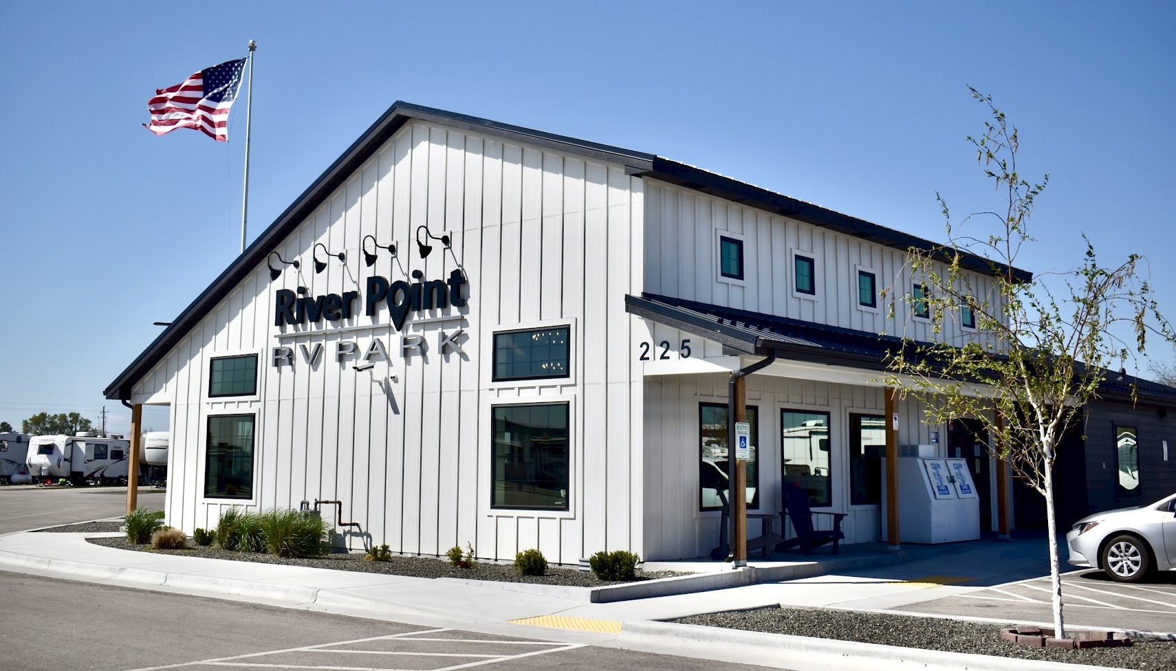 Rural-style building with a small sign &ldquo;River Point&rdquo; by Plan&hellip; flagpole with American flag; sunny day, parking lot in front.